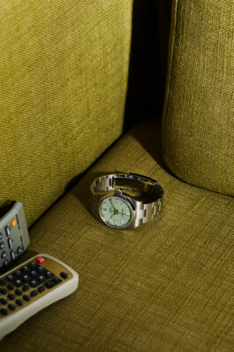 Photograph by Roderick Aichinger for Esquire Germany magazine. The image features a Rolex Datejust 41, reference 126334, with a mint green dial, displayed on a textured olive-green sofa alongside vintage remote controls. The composition highlights the luxury and unique colorway of the contemporary Rolex Datejust in a nostalgic home setting.