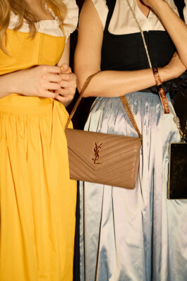 Two women stand together at Heidi Fest in Munich, wearing colorful dirndl dresses—one in yellow and one in pastel blue—with a YSL designer handbag. The image highlights the youthful, affluent 'jeunesse dorée' atmosphere of the Hofbräuhaus party. Photo by Roderick Aichinger for The New York Times, 2025.