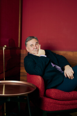 Ivan Krastev sits in a red armchair at Schloss Elmau during the “World in Pieces” symposium curated by him, leaning back in a contemplative pose. 