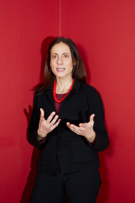 Nathalie Tocci stands in front of a red wall, gesturing while speaking during the “World in Pieces” symposium at Schloss Elmau.