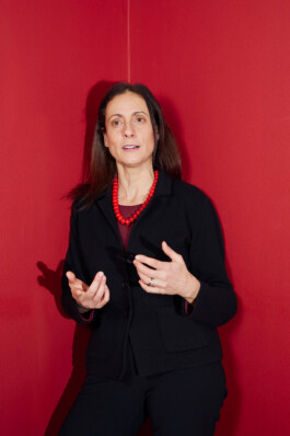 Nathalie Tocci stands in front of a red wall, gesturing while speaking during the “World in Pieces” symposium at Schloss Elmau.