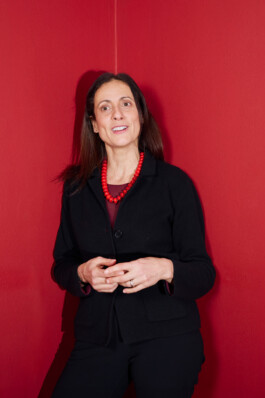 Nathalie Tocci stands in front of a red wall, gesturing while speaking during the “World in Pieces” symposium at Schloss Elmau.