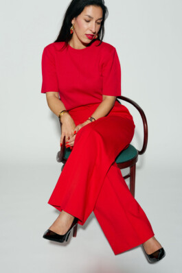 Tijen Onaran sits on a chair in a red outfit against a white background.