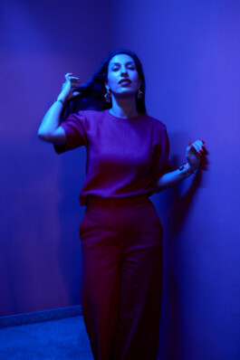 Tijen Onaran poses in a red outfit under blue lighting.