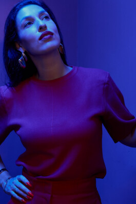 Tijen Onaran poses in a red outfit under blue lighting.