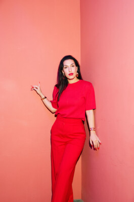 Tijen Onaran poses in a red outfit in front of a pink wall.